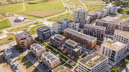 Luftbild eines nachhaltigen Wohnquartiers, kompakte Gebäude mit Gründächern, Solaranlagen und Grünflächen.
