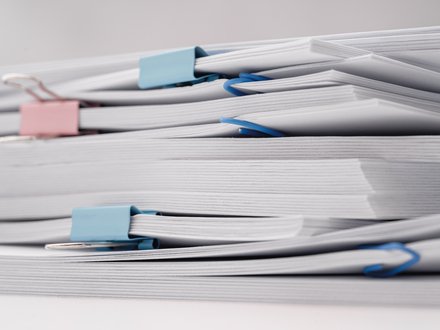 11:47     Nahaufnahme mehrerer Stapel weißer Dokumente auf weißem Hintergrund, mit blauen und rosa Büro- bzw. Foldbackklammern zusammengehalten.