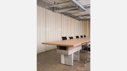 Große Tischtafel mit schwarzen Stühlen vor einem beigen Vorhang.