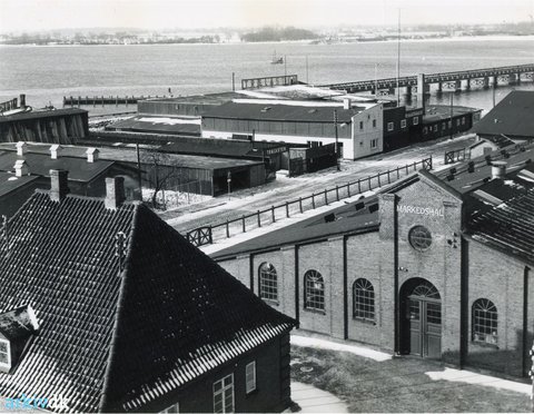 Schwarz-weiß-Fotografie der historischen Markedshallen mit Hafen- und Lagerbauten im Hintergrund.