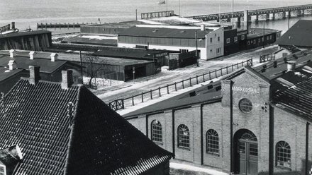 Schwarz-weiß-Fotografie der historischen Markedshallen mit Hafen- und Lagerbauten im Hintergrund.