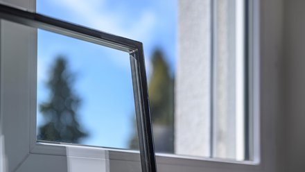 Behandschuhte Hand führt Isolierglasscheibe in Fensterrahmen ein.