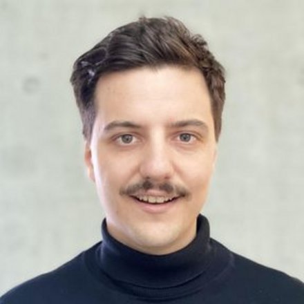 Porträt eines Mannes mit dunklem Haar und Schnurrbart vor hellem Hintergrund.