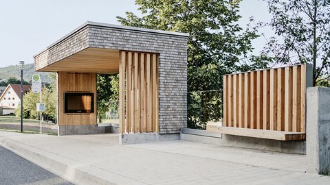 Moderner Wartebereich mit Holzverkleidung und Sitzbank an einer Bushaltestelle neben einer Straße