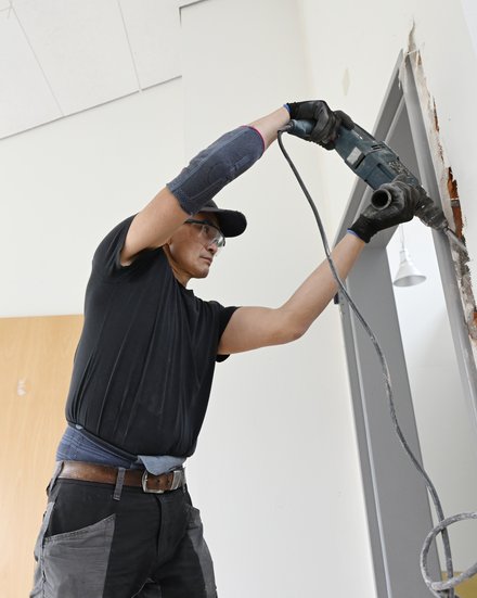 Handwerker mit Schutzbrille und Handschuhen arbeitet mit einem Bohrhammer am Türdurchbruch in einem Innenraum.