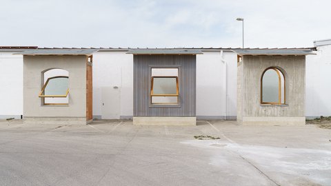 Drei verschiedene Architektur-Mock-ups (Fassadenausschnitte) stehen im Maßstab 1:1 auf einem Parkplatz. Sie zeigen unterschiedliche Fensterformen und Materialien wie Beton, Holzschalung und Putz.