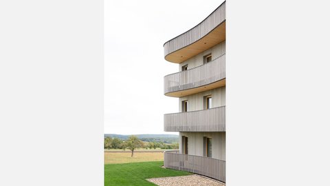 Detailansicht eines Wohnhauses mit abgerundeten Balkonen und Blick in die offene Landschaft mit Wiese und Bäumen.