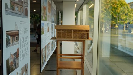 Holzmodell eines Gebäudes in einer Ausstellung mit begleitenden Architekturtafeln.