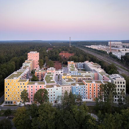 Luftaufnahme eines farbenfrohen Gebäudekomplexes, umgeben von Bäumen, in der Abenddämmerung.