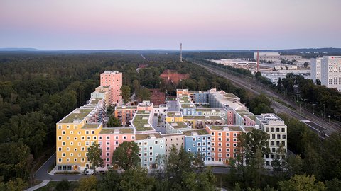 Luftaufnahme eines farbenfrohen Gebäudekomplexes, umgeben von Bäumen, in der Abenddämmerung.