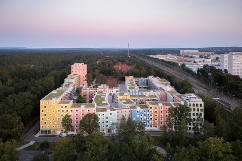 Luftaufnahme eines farbenfrohen Gebäudekomplexes, umgeben von Bäumen, in der Abenddämmerung.
