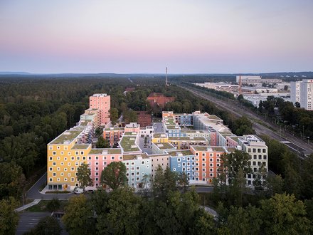 Luftaufnahme eines farbenfrohen Gebäudekomplexes, umgeben von Bäumen, in der Abenddämmerung.