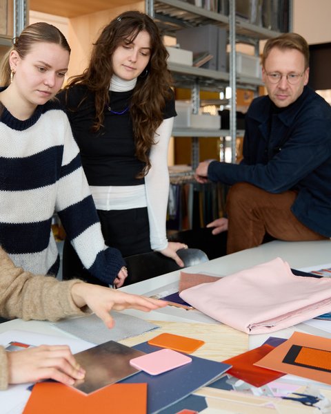 „Vier Personen begutachten und besprechen gemeinsam verschiedene Farb- und Materialmuster an einem großen Tisch in einem Kreativbüro.“