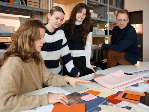 „Vier Personen begutachten und besprechen gemeinsam verschiedene Farb- und Materialmuster an einem großen Tisch in einem Kreativbüro.“
