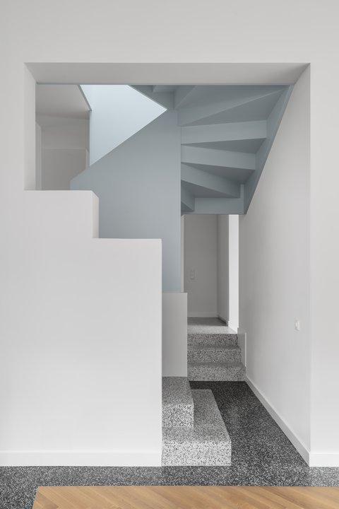 Minimalistisches Treppenhaus mit weiß verputzten Wänden, hellblauen Flächen und einer skulpturalen Treppe aus Terrazzostufen.