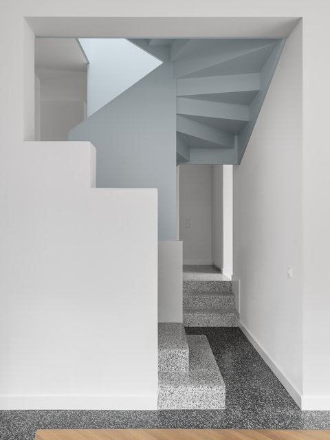 Minimalistisches Treppenhaus mit weiß verputzten Wänden, hellblauen Flächen und einer skulpturalen Treppe aus Terrazzostufen.