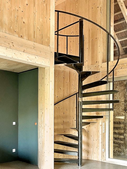 Schwarze Wendeltreppe aus Metall vor hellen Holzpaneelen in modernem Innenraum mit grün gestrichener Wand