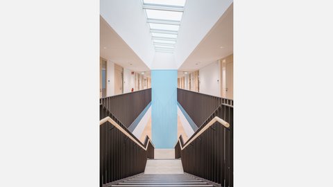 Helles Atrium mit zentraler Treppe, Oberlicht und offenen Galerien.
