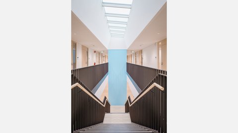 Helles Atrium mit zentraler Treppe, Oberlicht und offenen Galerien.