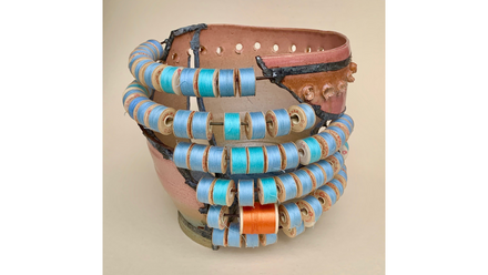 Gebrochene rosa Keramik; Reihen kleiner blauer Garnspulen auf Stäben um das Gefäß, eine Spule leuchtend orange.