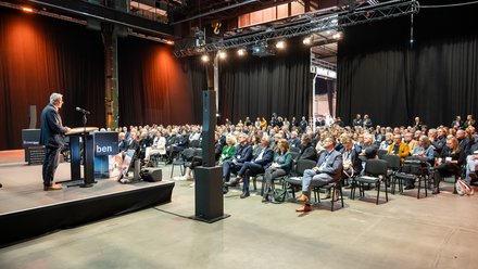 Plenum in Industriehalle: Redner am Pult vor großem Publikum bei einer Fachveranstaltung.