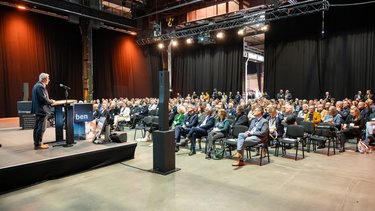 Plenum in Industriehalle: Redner am Pult vor großem Publikum bei einer Fachveranstaltung.