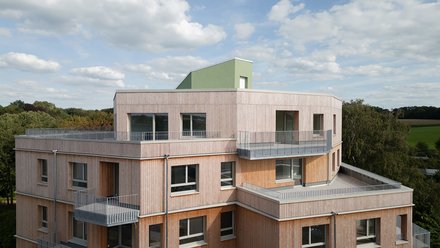 Außenansicht eines Holzgebäudes mit mehreren Balkonen, das ein zeitgenössisches architektonisches Design zeigt.