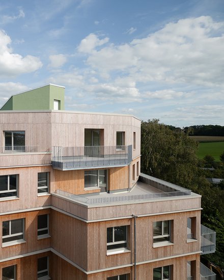 Außenansicht eines Holzgebäudes mit mehreren Balkonen, das ein zeitgenössisches architektonisches Design zeigt.