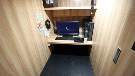 Schmale Kabine mit Computerarbeitsplatz, Monitor, Tastatur und gepolsterter Liege.