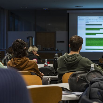 Ein Lehrsaal mit mehreren Studierenden, die auf eine Leinwand schauen
