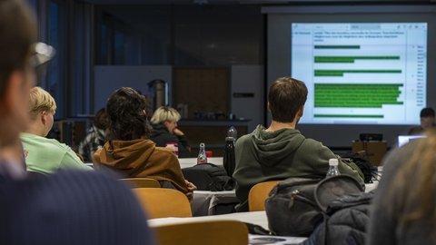 Ein Lehrsaal mit mehreren Studierenden, die auf eine Leinwand schauen
