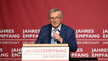 Redner im blauen Anzug am Pult vor rotem Hintergrund mit Schriftzug „JAHRESEMPFANG DER WIRTSCHAFT“; spricht in zwei Mikrofone und gestikuliert.
