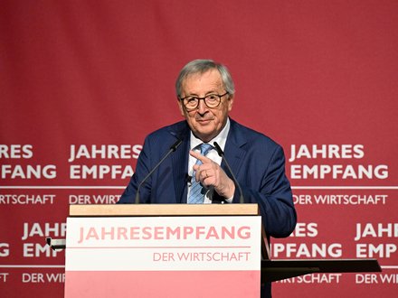 Redner im blauen Anzug am Pult vor rotem Hintergrund mit Schriftzug „JAHRESEMPFANG DER WIRTSCHAFT“; spricht in zwei Mikrofone und gestikuliert.