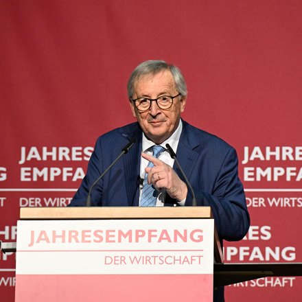Redner im blauen Anzug am Pult vor rotem Hintergrund mit Schriftzug „JAHRESEMPFANG DER WIRTSCHAFT“; spricht in zwei Mikrofone und gestikuliert.