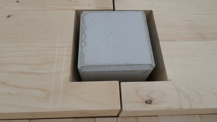 Draufsicht auf Anschlussdetail: Quadratische Betonstütze ragt durch L-förmig ausgesparte Öffnungen einer massiven Holzdecke.