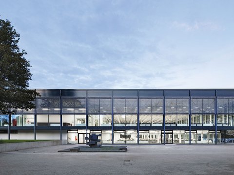 Moderne Glasfassade eines Gebäudes mit beleuchtetem Innenraum.