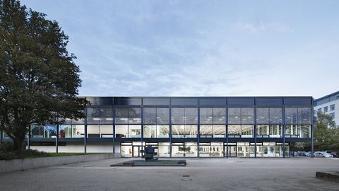 Moderne Glasfassade eines Gebäudes mit beleuchtetem Innenraum.