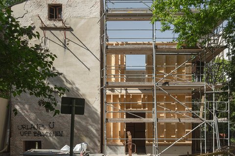Ansicht einer Baustelle mit Blick auf einen alten Seitenflügel umrahmt von Bäumen