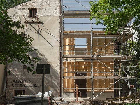 Ansicht einer Baustelle mit Blick auf einen alten Seitenflügel umrahmt von Bäumen