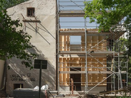 Ansicht einer Baustelle mit Blick auf einen alten Seitenflügel umrahmt von Bäumen