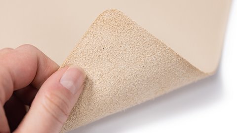 Hand hält eine Ecke eines dünnen, beigen, texturierten Materials