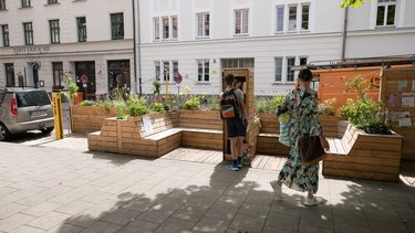 Mit Holzmöbeln gestaltetes Parklet dient als Tauschregal für Bücher in einer Fußgängerzone.