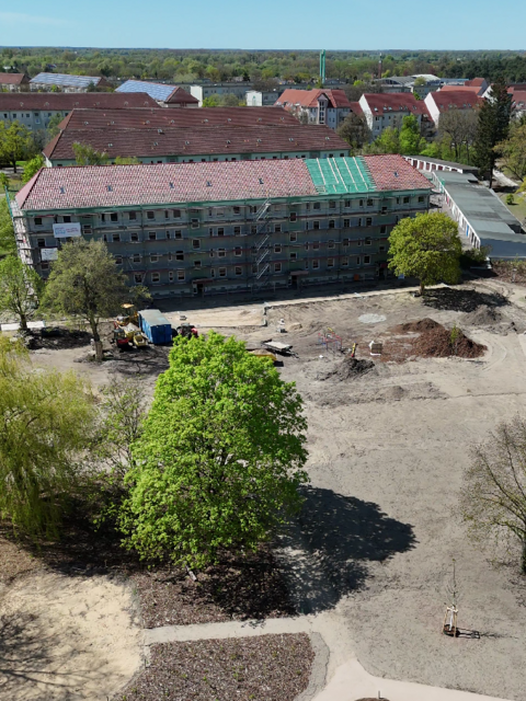 Luftaufnahme eines Modellquartiers mit saniertem Wohngebäude, neu angelegten Wegen und Grünflächen.