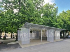 „Architektur-Rendering eines leichten, halboffenen Pavillons mit transluzenten Schiebewänden unter großen Bäumen in einer Parkanlage.“