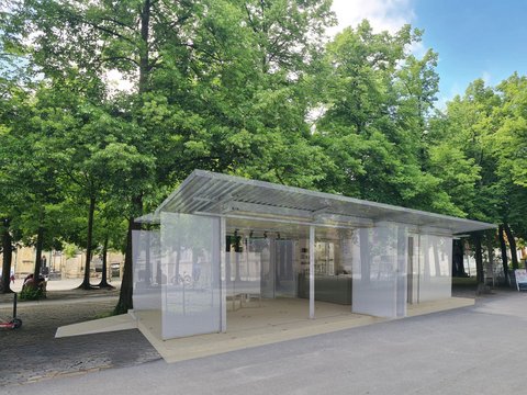 „Architektur-Rendering eines leichten, halboffenen Pavillons mit transluzenten Schiebewänden unter großen Bäumen in einer Parkanlage.“