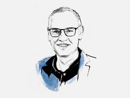 Schwarz-weiße Porträtzeichnung einer lächelnden erwachsenen Person mit Kurzhaar und Brille, in dunklem Hemd und Jacke; blaue Aquarellakzente auf Schultern.