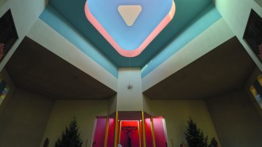 Kircheninnenraum mit Altar, Kreuz und farbiger Decke.