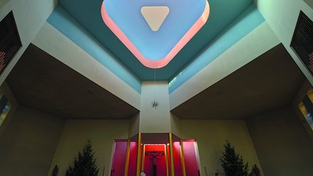 Kircheninnenraum mit Altar, Kreuz und farbiger Decke.