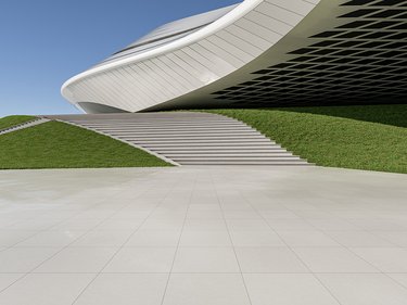 Freitreppe mit grasbedeckten Seitenflächen vor einem modernen, geschwungenen Gebäude mit weißer Fassade und dunklem Unterbau.