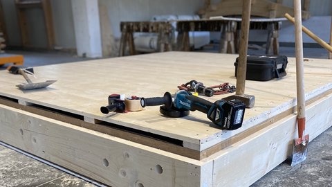 Verschlossenes Holzbauelement in der Werkhalle; auf der Deckplatte liegen Akkuschrauber, Hammer und weiteres Handwerkzeug.